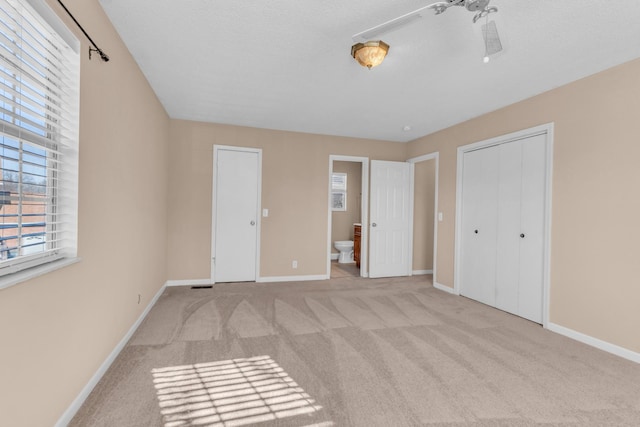 unfurnished bedroom featuring connected bathroom, a closet, and light carpet