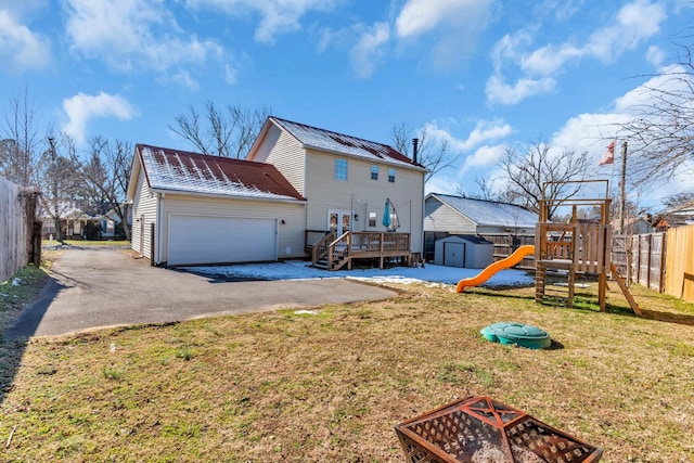 rear view of house with a deck, a playground, a garage, a yard, and a storage unit