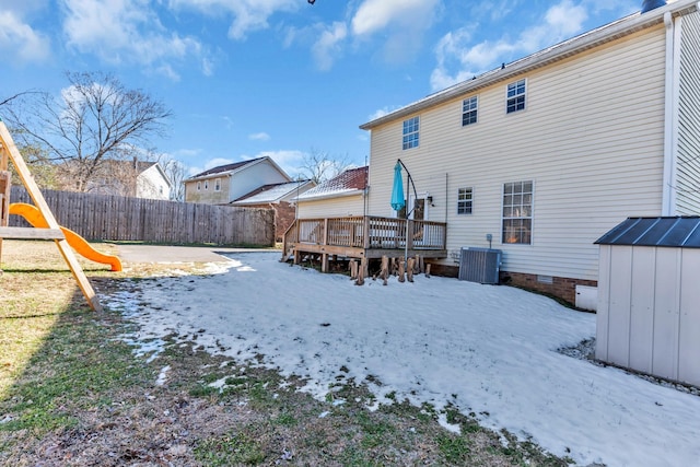 snow covered rear of property featuring cooling unit, a playground, a storage unit, and a wooden deck