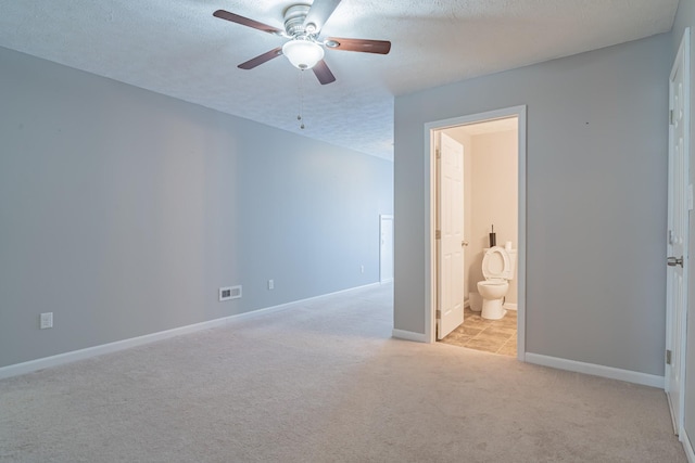 interior space featuring ceiling fan, light colored carpet, connected bathroom, and a textured ceiling