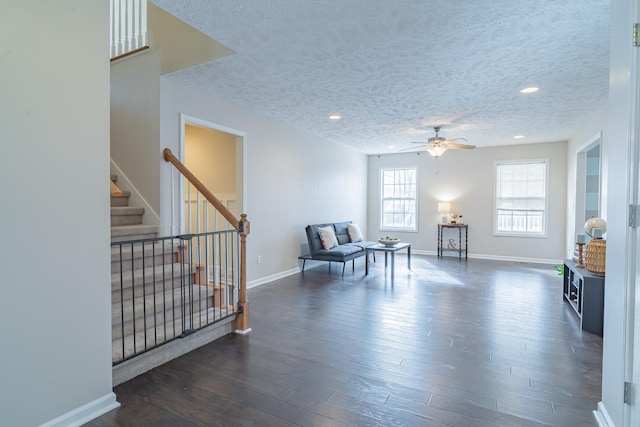 living area with ceiling fan, dark wood-type flooring, and a textured ceiling