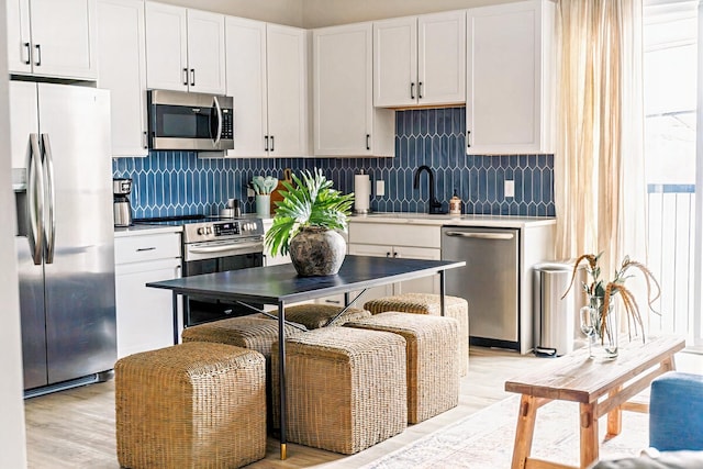 kitchen with stainless steel appliances, sink, white cabinetry, light wood-type flooring, and tasteful backsplash