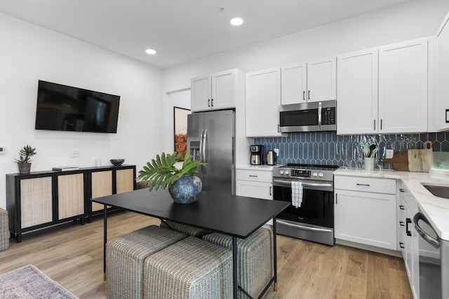 kitchen featuring backsplash, white cabinetry, stainless steel appliances, and light wood-type flooring