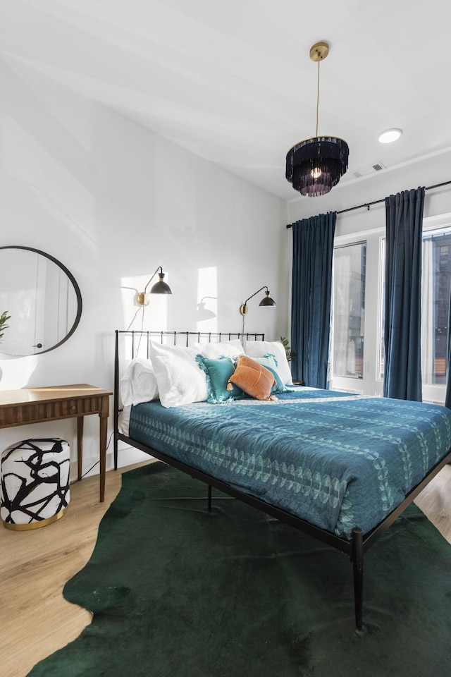 bedroom with wood finished floors, visible vents, and an inviting chandelier