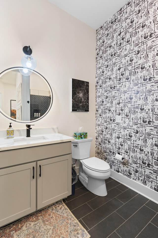 bathroom with an accent wall, wallpapered walls, vanity, baseboards, and toilet