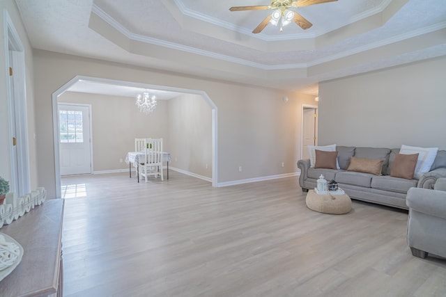 living room featuring ceiling fan with notable chandelier, crown molding, a raised ceiling, and light hardwood / wood-style flooring