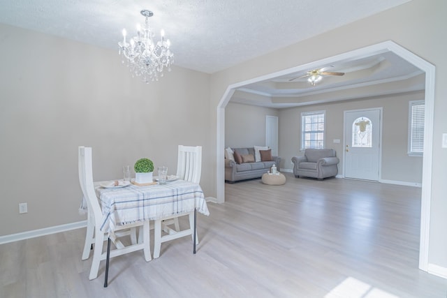 dining space with a raised ceiling, wood-type flooring, ornamental molding, a textured ceiling, and ceiling fan with notable chandelier