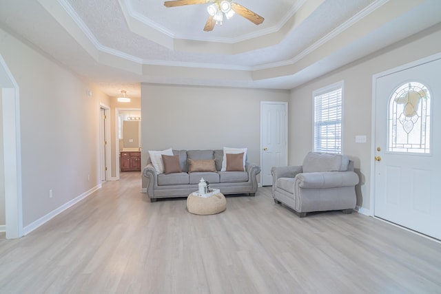 living room with a raised ceiling, ceiling fan, crown molding, and light hardwood / wood-style flooring