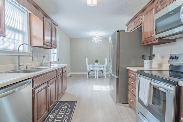 kitchen with sink, light wood-type flooring, hanging light fixtures, a notable chandelier, and appliances with stainless steel finishes