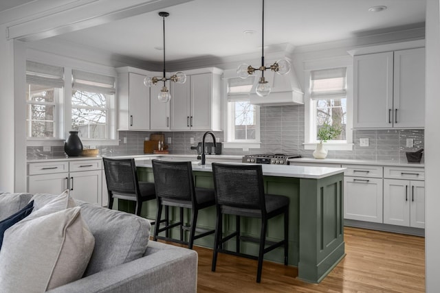 kitchen with light hardwood / wood-style floors, decorative light fixtures, white cabinetry, and a kitchen island with sink