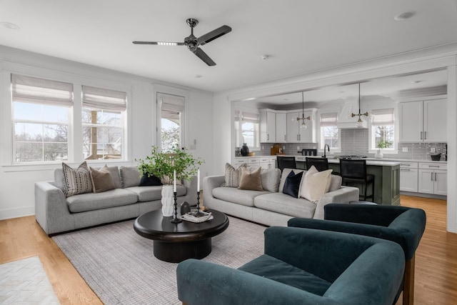 living room featuring ceiling fan with notable chandelier, light hardwood / wood-style floors, crown molding, and sink