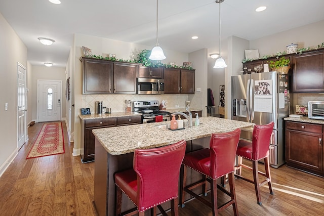 kitchen with sink, hanging light fixtures, dark brown cabinetry, a center island with sink, and appliances with stainless steel finishes