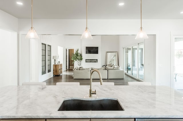 kitchen featuring light stone counters, an island with sink, decorative light fixtures, and sink