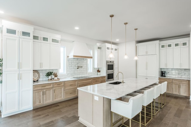 kitchen with sink, white cabinetry, light stone countertops, a center island with sink, and custom exhaust hood