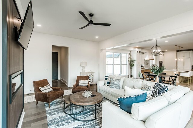 living room with wood-type flooring, sink, and ceiling fan with notable chandelier