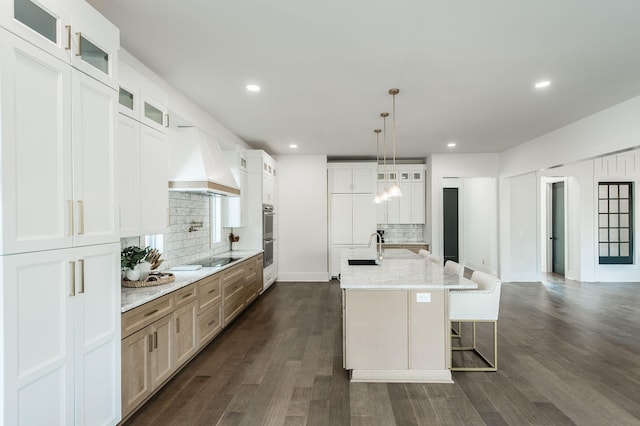 kitchen featuring tasteful backsplash, dark hardwood / wood-style flooring, an island with sink, custom range hood, and white cabinets