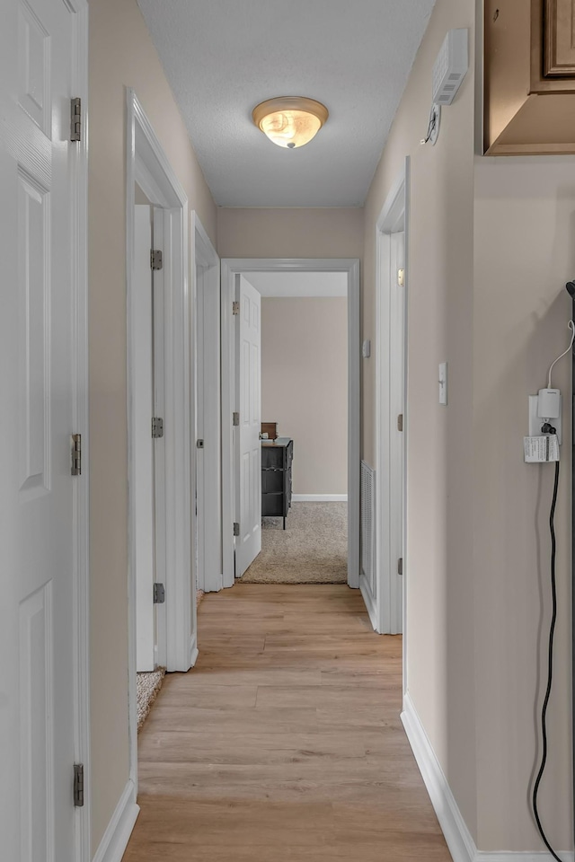 hallway with a textured ceiling and light hardwood / wood-style flooring