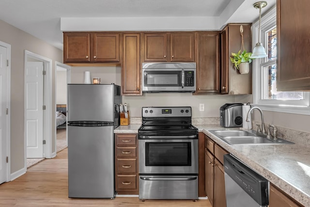 kitchen featuring appliances with stainless steel finishes, light hardwood / wood-style flooring, pendant lighting, and sink