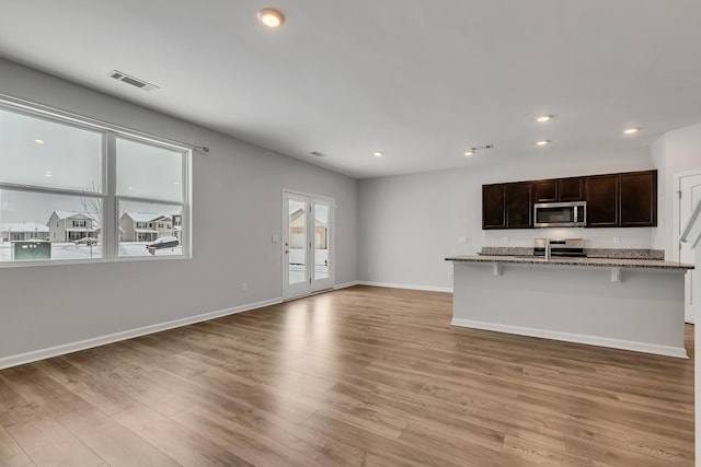 kitchen featuring stainless steel appliances, a kitchen bar, light hardwood / wood-style flooring, light stone countertops, and a kitchen island with sink