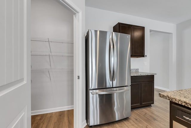 kitchen with dishwasher, light hardwood / wood-style floors, stainless steel fridge, light stone counters, and dark brown cabinets