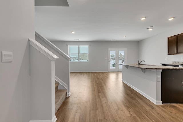 interior space featuring light stone counters, a kitchen bar, light wood-type flooring, dark brown cabinetry, and sink