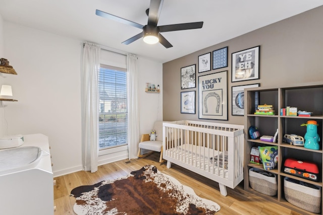 bedroom featuring ceiling fan, a crib, and wood-type flooring