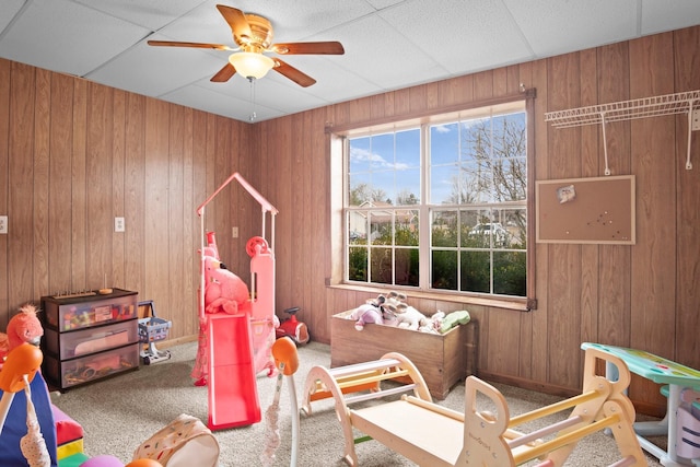 recreation room with ceiling fan, carpet floors, and wood walls