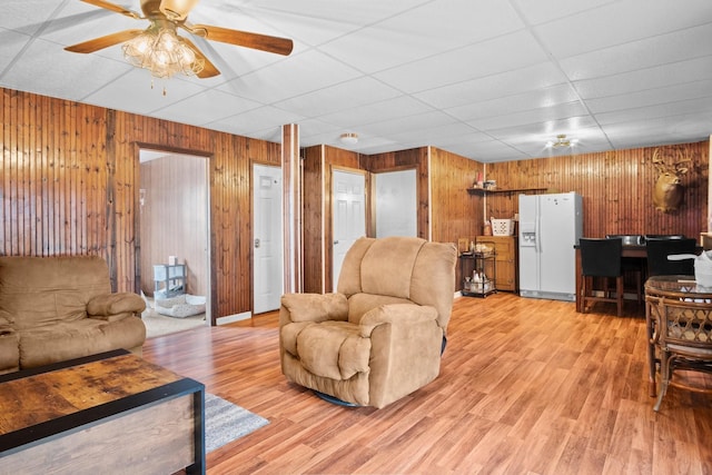 living room with ceiling fan, wooden walls, a paneled ceiling, and light hardwood / wood-style flooring