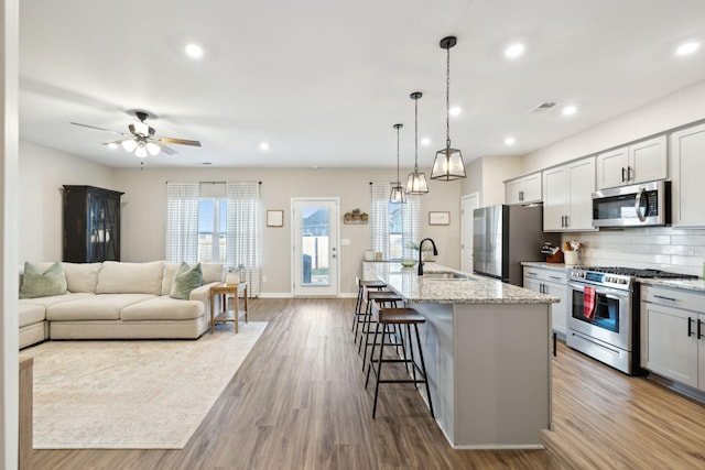 kitchen with light stone countertops, stainless steel appliances, a breakfast bar, a kitchen island with sink, and backsplash