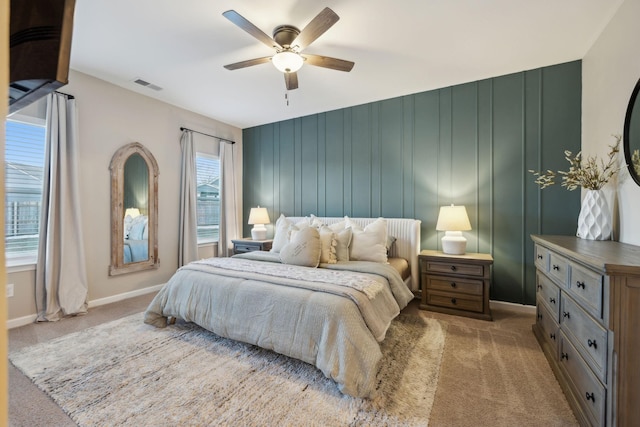 bedroom featuring light colored carpet, wood walls, ceiling fan, and multiple windows