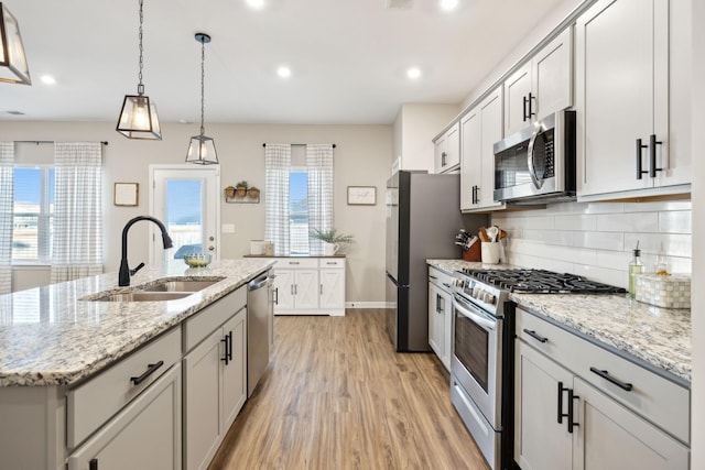 kitchen with appliances with stainless steel finishes, an island with sink, light wood-type flooring, pendant lighting, and sink