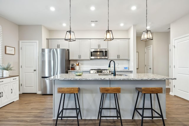 kitchen with appliances with stainless steel finishes, hanging light fixtures, sink, and a center island with sink