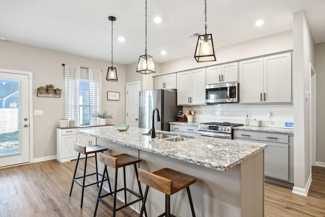 kitchen featuring hanging light fixtures, stainless steel appliances, a kitchen island with sink, backsplash, and a kitchen breakfast bar