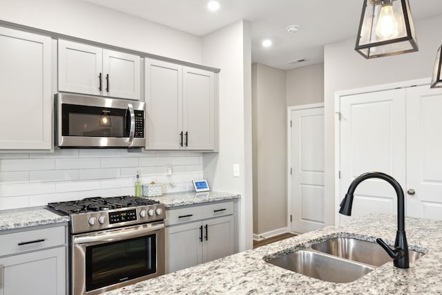 kitchen with appliances with stainless steel finishes, hanging light fixtures, light stone countertops, sink, and backsplash