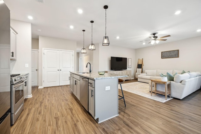 kitchen with light stone countertops, decorative light fixtures, stainless steel appliances, a kitchen island with sink, and a breakfast bar area