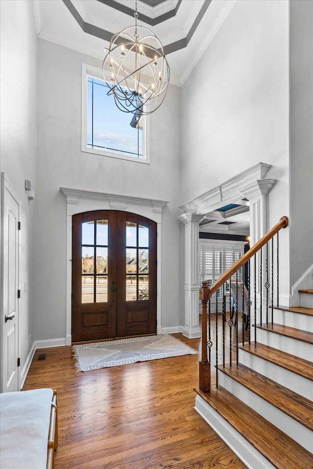 entryway featuring a raised ceiling, a chandelier, wood-type flooring, ornamental molding, and french doors