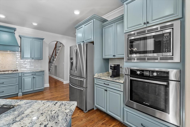 kitchen with custom exhaust hood, appliances with stainless steel finishes, blue cabinetry, dark hardwood / wood-style flooring, and tasteful backsplash