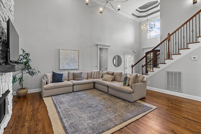 living room featuring an inviting chandelier, a towering ceiling, dark hardwood / wood-style flooring, crown molding, and a stone fireplace