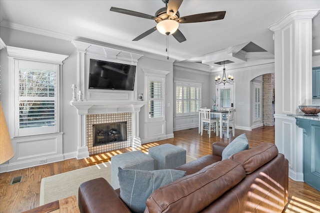 living room with ceiling fan with notable chandelier, a tiled fireplace, crown molding, and dark hardwood / wood-style floors