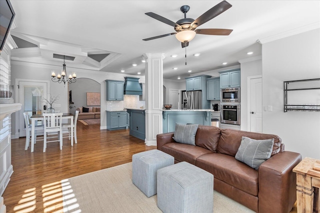 living room featuring ceiling fan with notable chandelier, decorative columns, light wood-type flooring, and crown molding