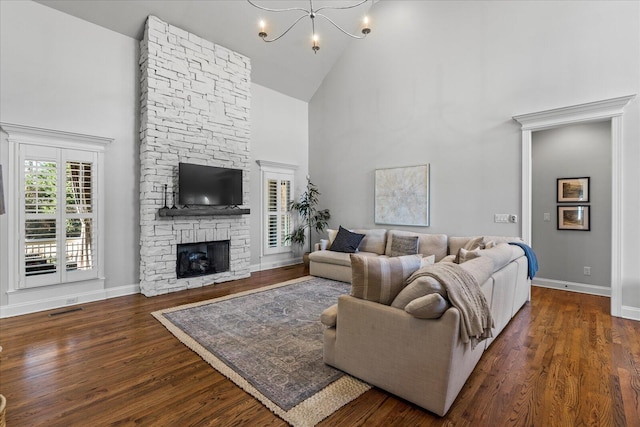 living room featuring dark wood-type flooring, high vaulted ceiling, a chandelier, and a stone fireplace