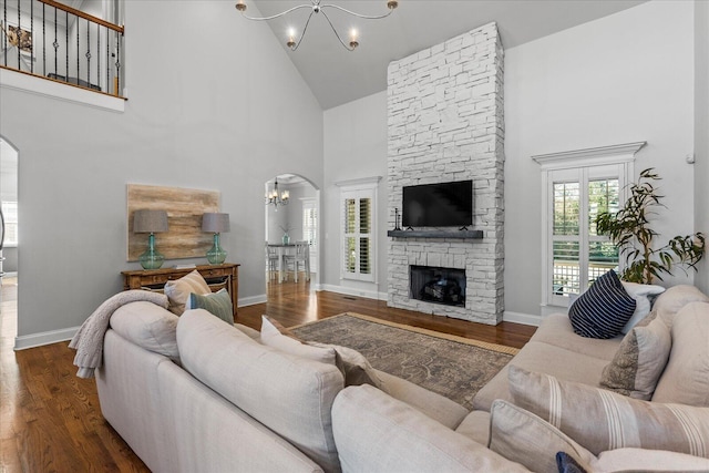 living room with high vaulted ceiling, dark hardwood / wood-style floors, a chandelier, and a stone fireplace