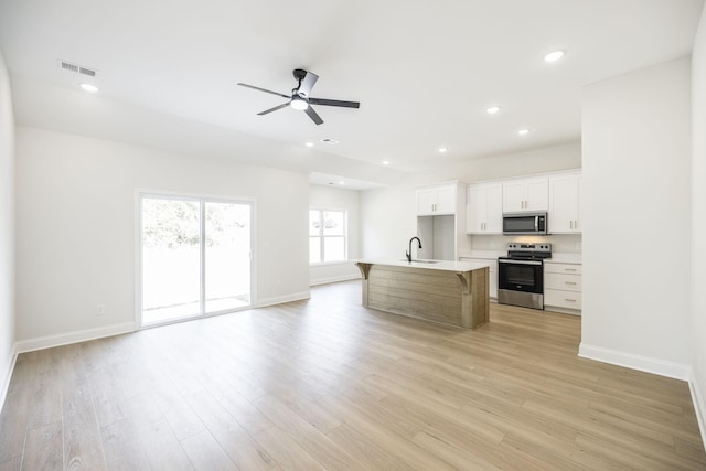 kitchen with light hardwood / wood-style flooring, stainless steel appliances, a kitchen island with sink, white cabinets, and sink