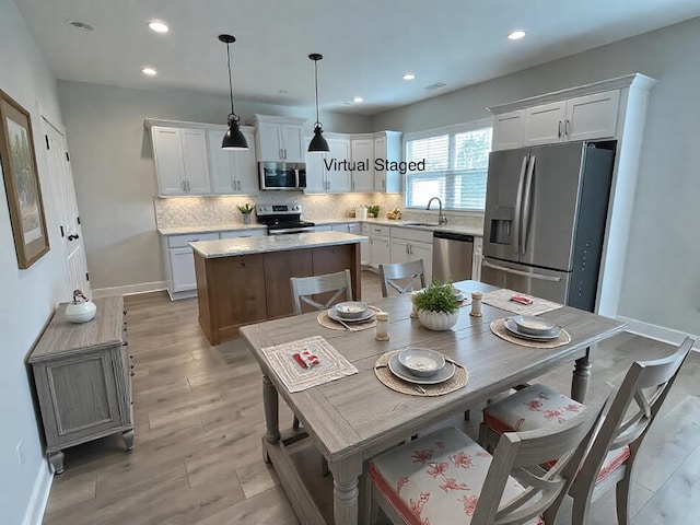 kitchen with appliances with stainless steel finishes, hanging light fixtures, white cabinets, and a kitchen island