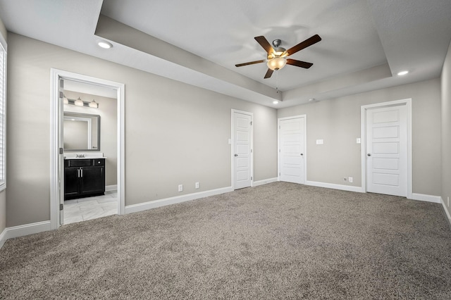 unfurnished bedroom with ensuite bath, ceiling fan, a tray ceiling, and light colored carpet