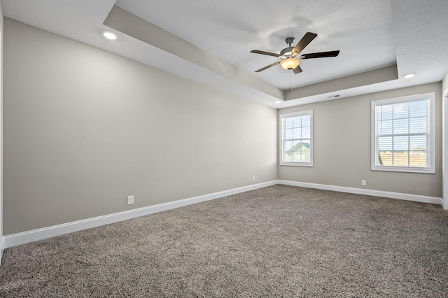 empty room featuring ceiling fan, a raised ceiling, and carpet