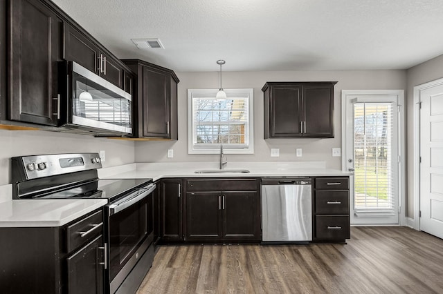 kitchen with wood-type flooring, stainless steel appliances, a textured ceiling, pendant lighting, and sink