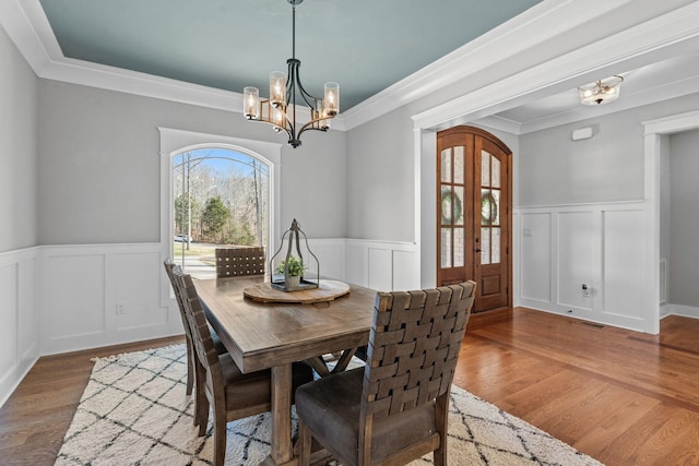 dining room featuring wood-type flooring, an inviting chandelier, ornamental molding, and french doors