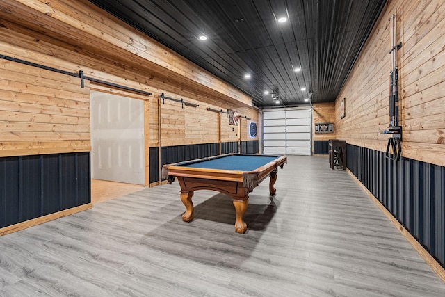 rec room featuring pool table, light hardwood / wood-style flooring, a barn door, and wood walls