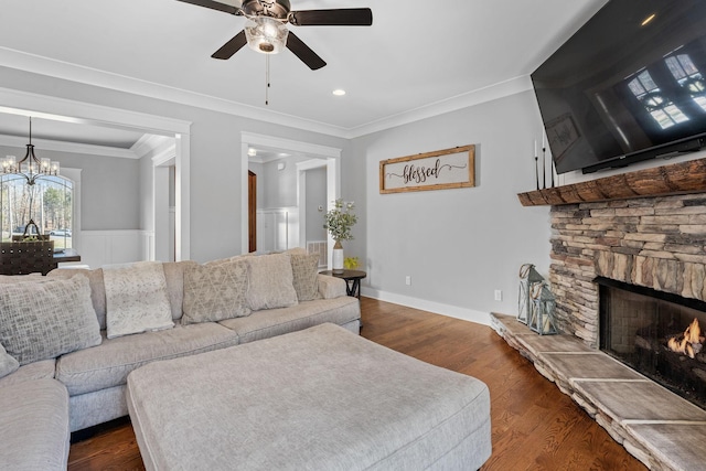 living room with ceiling fan with notable chandelier, dark hardwood / wood-style flooring, ornamental molding, and a stone fireplace